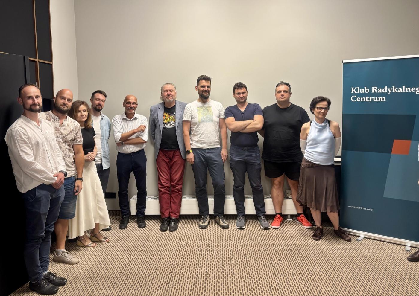 Dziesięć osób stoi w rzędzie przy ścianie sali konferencyjnej, obok banera z napisem „Klub Radykalnego Centrum". Zdjęcie grupowe po pierwszym spotkaniu klubu wrocławskiego.